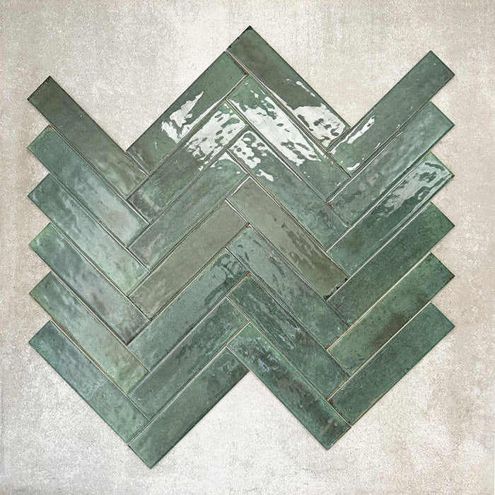 Allegra Green Gloss Brick ceramic tiles in a 6 × 25cm format, arranged in a herringbone pattern to showcase the deep green colour, high-gloss finish and subtle handmade-style surface variation.