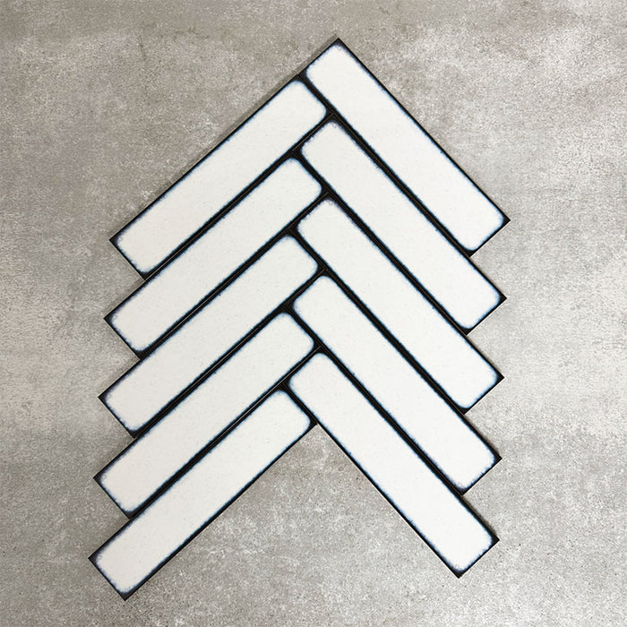 Alchemy Magma White 6.5×30cm ceramic wall tiles arranged in a herringbone pattern with a glossy white finish.