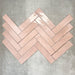 Nomad Rose brick wall tiles in a 6 × 24.6cm format, shown laid together in a herringbone layout to highlight the soft pink tone, gloss finish and subtle surface variation.