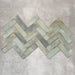 Saigon Celadon Green Brick Wall tiles laid in a herringbone pattern, showcasing Moroccan-style 5.1 × 16.1cm glossy ceramic tiles with soft green and blue-grey tonal variation.