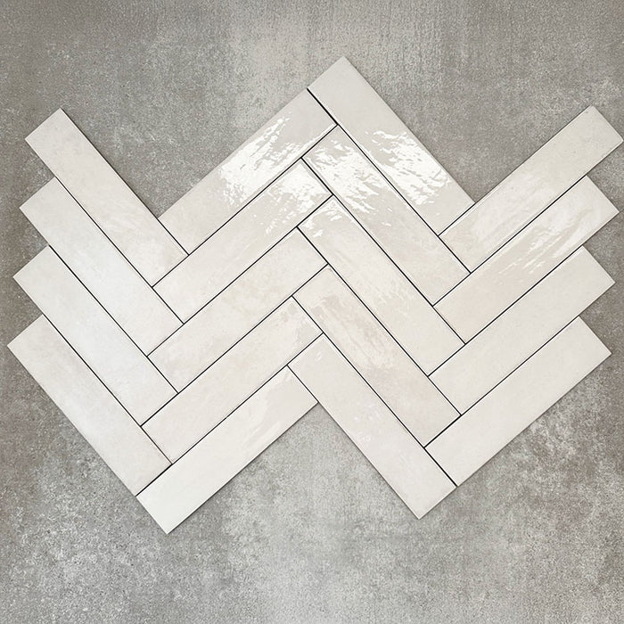 Nomad White brick wall tiles in a 6 × 24.6cm format, shown laid together in a herringbone to highlight the soft white colour, gloss finish and subtle surface variation.