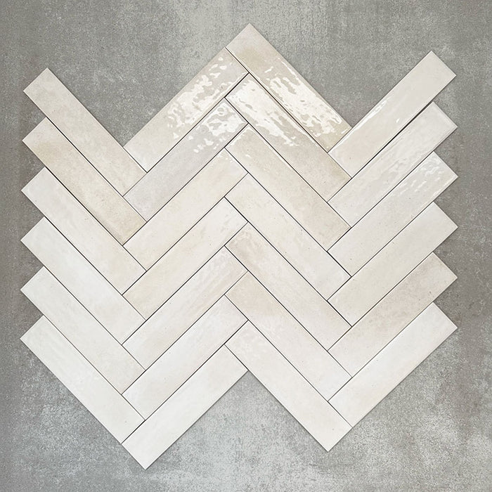 Allegra Blanca Gloss Brick ceramic tiles in a 6 × 25cm format, arranged in a herringbone pattern to showcase the glossy white finish and subtle handmade-style variation.