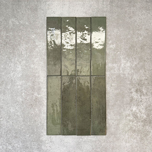 Nomad Sage Green brick wall tiles in a 6 × 24.6cm format, shown in a flat lay arrangement with a glossy, lightly textured surface and deep green tones, ideal for creating an industrial-style wall finish.
