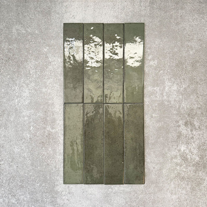 Nomad Sage Green brick wall tiles in a 6 × 24.6cm format, shown in a flat lay arrangement with a glossy, lightly textured surface and deep green tones, ideal for creating an industrial-style wall finish.