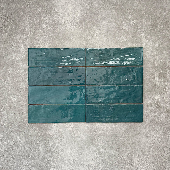 Flat lay of Zellige Peacock Green 6.5×20cm Moroccan-style ceramic brick tiles, showcasing deep blue-green tones, a glossy handmade-look glaze and natural tonal variation on a neutral background.
