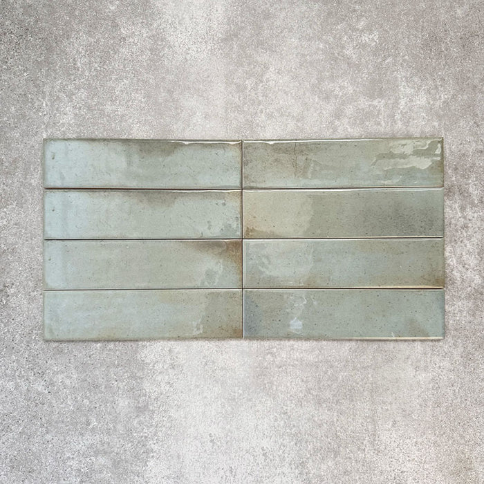 Allegra Celadon Green Gloss Brick ceramic tiles in a 6 × 25cm format, laid horizontally to highlight the soft green tones, glossy finish and subtle handmade-style surface variation.