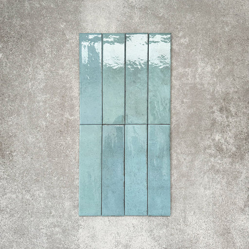 Nomad Aquamarine brick wall tiles in a 6 × 24.6cm format, shown laid vertically with a glossy, lightly textured surface and soft blue-green tones, creating an industrial-style look.