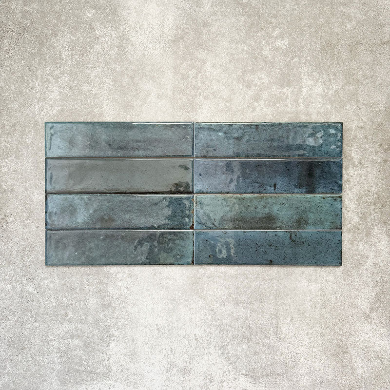 Allegra Blue Gloss Brick ceramic tiles in a 6 × 25cm format, laid horizontally to highlight the deep blue tones, glossy finish and subtle handmade-style surface variation.