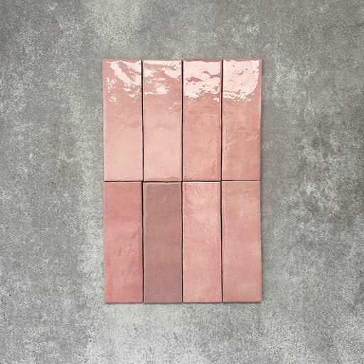 Flat lay of Zellige Rose Pink Brick 6.5 × 20cm Moroccan-style ceramic tiles, shown in soft blush, dusty rose and terracotta pink tones with gentle tonal variation and lightly uneven edges, arranged in a vertical brick layout on a textured grey background to showcase the handcrafted zellige-effect glaze.