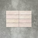 Flat lay of Zellige Pink Mist Brick 6.5 × 20cm Moroccan-style ceramic tiles in soft pale pink and blush tones, arranged in a horizontal brick layout on a textured grey background, showcasing the glossy glaze, gentle tonal variation and handcrafted zellige-effect finish.
