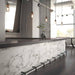 Bar and dining setting featuring Hudson Calacatta Matt Marble 60 × 60cm porcelain wall tiles, styled across the counter front to showcase soft grey veining on a clean white base, paired with dark worktops, industrial lighting, and polished concrete for a refined, contemporary contrast.