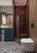 Bathroom setting featuring Shards Terrazzo Nero 59x118cm matt porcelain wall and floor tiles, showcasing a bold black base with contrasting white aggregate, paired with deep red brick tiles, blue cabinetry and brass fittings for a striking, contemporary finish.