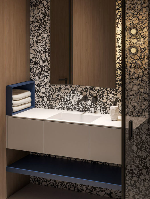 Bathroom setting featuring Shards Terrazzo Nero 59x118cm matt porcelain wall and floor tiles, showcasing a bold black base with contrasting white aggregate, paired with warm wood cabinetry, matte black fittings and soft ambient lighting.
