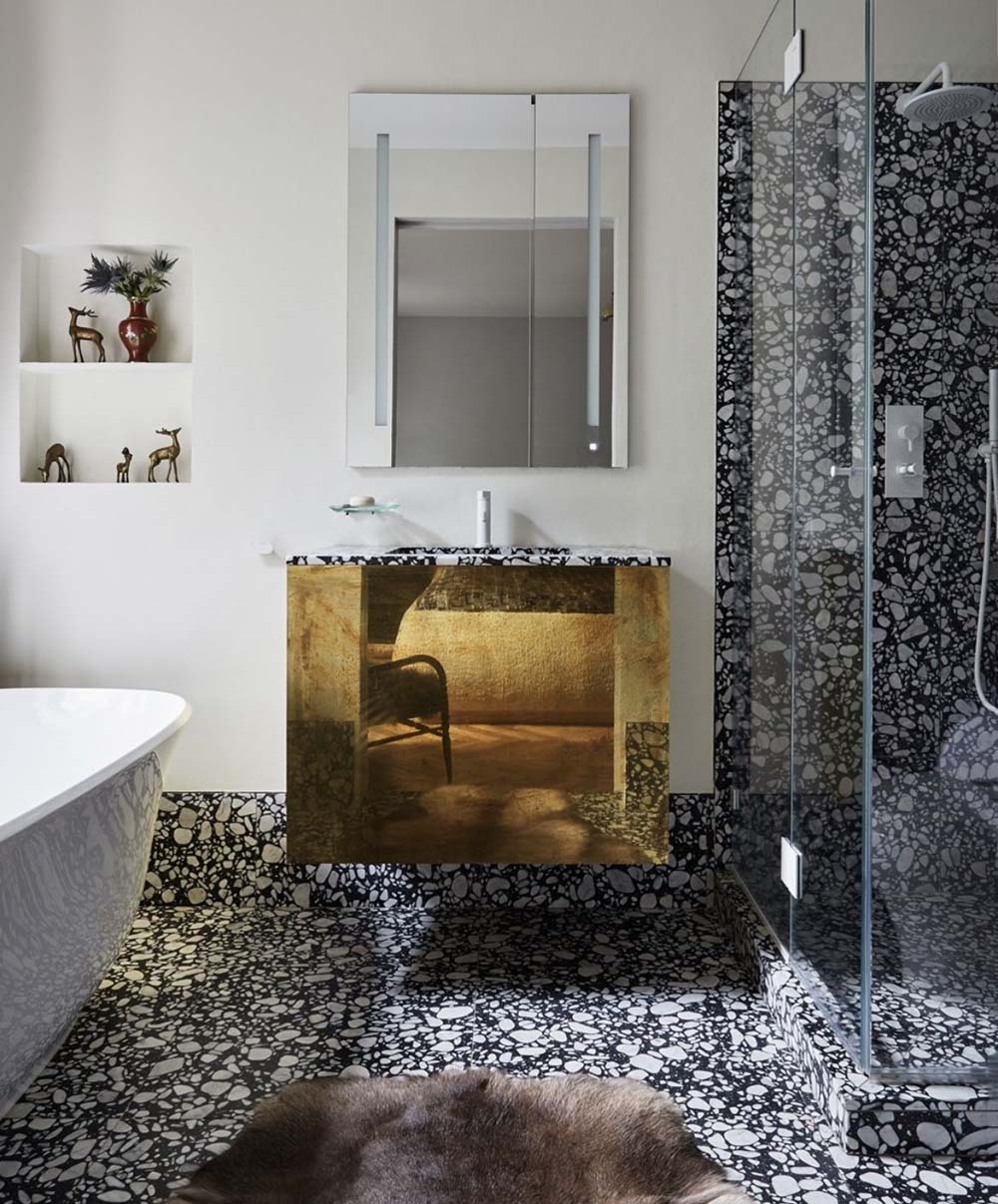 Bathroom setting featuring Shards Terrazzo Nero 59x59cm matt porcelain wall and floor tiles, showcasing a bold terrazzo effect with large white stone fragments set against a deep black base, used across the floor and shower enclosure to create a seamless, immersive finish, paired with a statement vanity, soft neutral walls and warm metallic accents for a refined, design-led look.