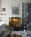Bathroom setting featuring Shards Terrazzo Nero 59x59cm matt porcelain wall and floor tiles, showcasing a bold terrazzo effect with large white stone fragments set against a deep black base, used across the floor and shower enclosure to create a seamless, immersive finish, paired with a statement vanity, soft neutral walls and warm metallic accents for a refined, design-led look.