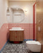 Bathroom setting featuring Shards Terrazzo Nero 59x59cm matt porcelain floor tiles, showcasing a bold terrazzo effect with large white stone fragments set against a deep black base, used across the floor to ground the space, paired with soft pink wall tiles, warm wood finishes and red accents for a playful yet design-led contrast.