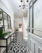 Hallway interior featuring Dorset Tile Black & White 25x25cm Victorian-style patterned floor tiles, styled with white panelled walls, staircase, black metal console table, and decorative accessories in a bright, classic entrance space.