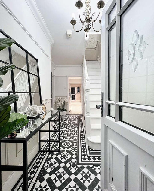 Hallway interior featuring Dorset Tile Black & White 25x25cm Victorian-style patterned floor tiles, styled with white panelled walls, staircase, black metal console table, and decorative accessories in a bright, classic entrance space.