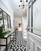 Hallway interior featuring Dorset Tile Black & White 25x25cm Victorian-style patterned floor tiles, styled with white panelled walls, staircase, black metal console table, and decorative accessories in a bright, classic entrance space.