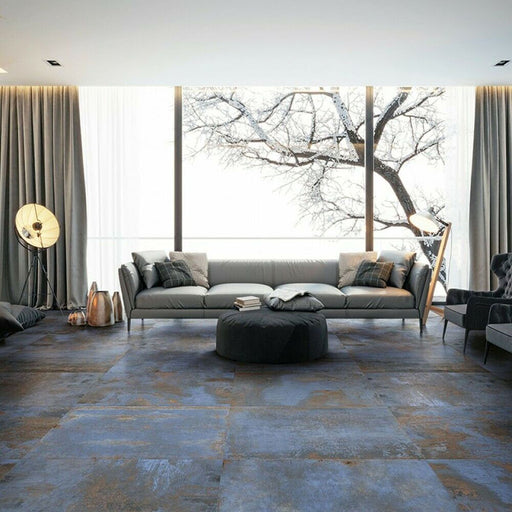 Living room interior featuring Iron Blue Oxide Metallic 30 × 60cm porcelain floor tiles, styled with deep blue tones layered with warm oxidised variation and a softly textured metallic effect surface, paired with contemporary furnishings and soft neutral fabrics for a moody, industrial-inspired finish.