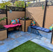 Outdoor patio featuring Iron Blue Oxide Metallic 60 × 60cm porcelain floor tiles, styled with deep blue tones and warm oxidised variation, creating a textured, industrial-inspired surface, paired with timber seating, vibrant cushions, and greenery for a bold yet inviting garden setting.
