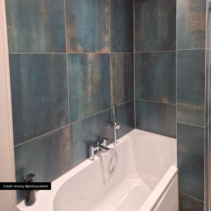 Bathroom interior featuring Iron Cuprum Oxide Metallic 60 × 60cm porcelain wall tiles, showcasing deep blue-green tones with warm coppery oxidation and soft tonal variation, paired with a white bath and chrome fittings for a striking, industrial-inspired finish.