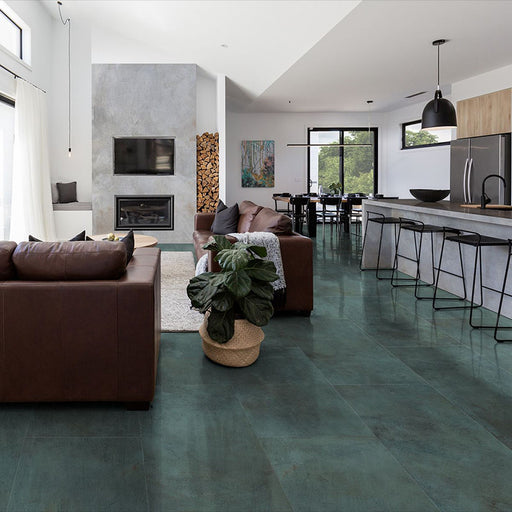 Open-plan living and kitchen space featuring Iron Emerald Green Oxide Metallic 30 × 60cm porcelain floor tiles, showcasing rich green tones with subtle tonal variation and a soft metallic effect, paired with warm leather seating, natural wood, and modern black accents for a bold yet balanced contemporary interior.