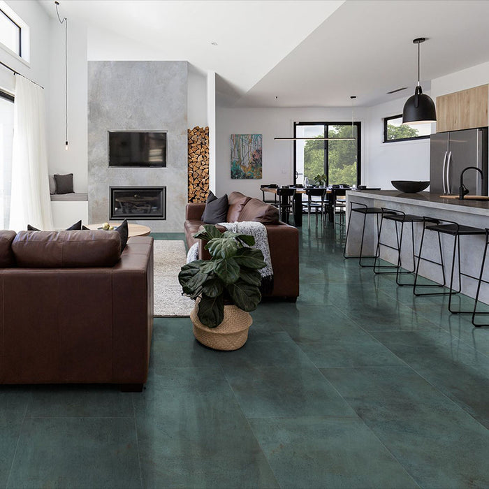 Open-plan living and kitchen space featuring Iron Emerald Green Oxide Metallic 30 × 60cm porcelain floor tiles, showcasing rich green tones with subtle tonal variation and a soft metallic effect, paired with warm leather seating, natural wood, and modern black accents for a bold yet balanced contemporary interior.