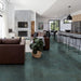 Open-plan living and kitchen space featuring Iron Emerald Green Oxide Metallic 30 × 60cm porcelain floor tiles, showcasing rich green tones with subtle tonal variation and a soft metallic effect, paired with warm leather seating, natural wood, and modern black accents for a bold yet balanced contemporary interior.