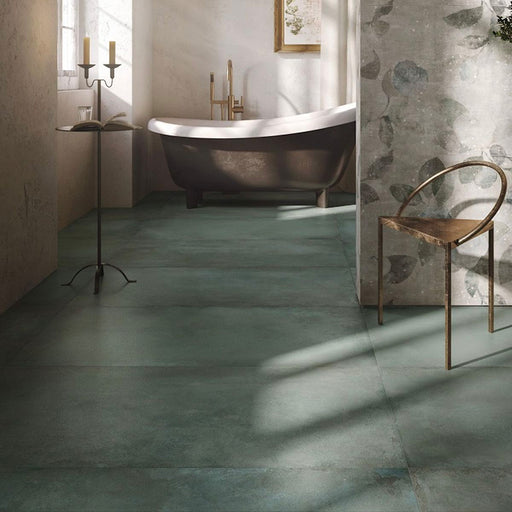 Bathroom interior featuring Iron Emerald Green Oxide Metallic 60 × 120cm porcelain floor tiles, styled with deep green tonal variation and a softly textured, metallic effect surface, paired with a freestanding bath, brass fittings, and warm neutral walls for a calm, contemporary finish.