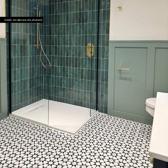 Bathroom interior featuring Zellige Royal Green 6.5x20cm Moroccan-style brick tiles installed vertically in a walk-in shower, styled with brushed brass fittings, sage panelling, and patterned black and white floor tiles.