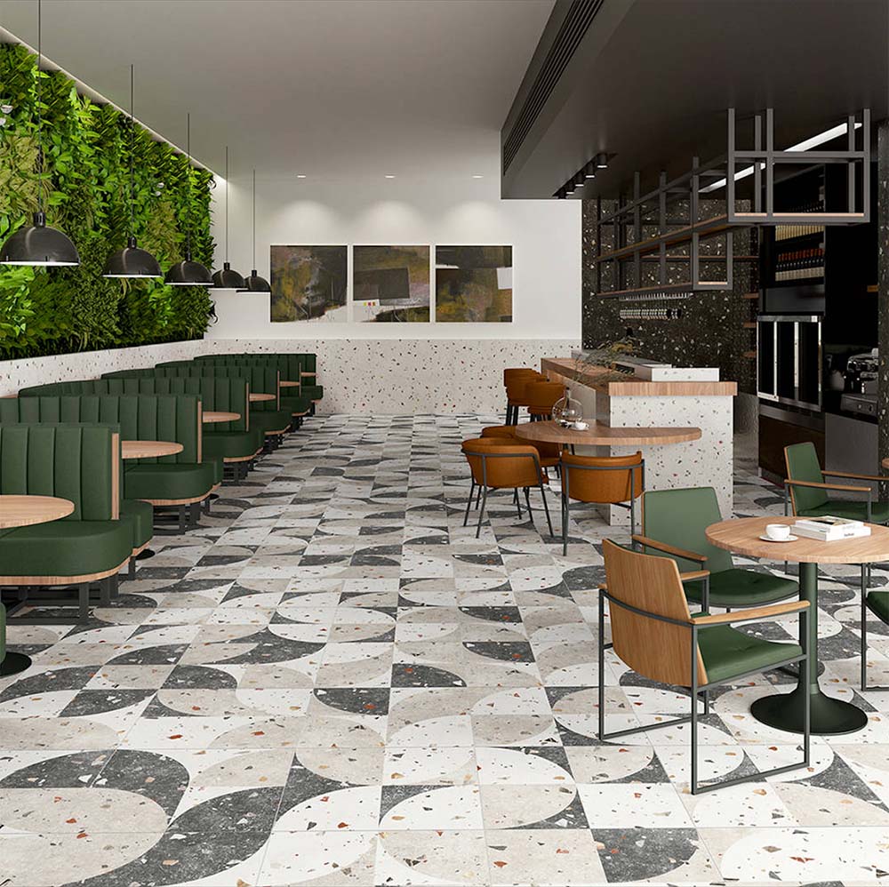 Café interior featuring Jericho Decor Terrazzo 66 × 66cm porcelain wall and floor tiles, combining a soft terrazzo base with bold geometric patterning in contrasting tones, paired with green seating, warm wood furniture, and contemporary lighting for a playful yet refined setting.