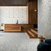 Hotel reception interior featuring Jericho Silver Terrazzo Hexagon 25 × 22cm porcelain wall and floor tiles, with a soft grey base and scattered multicoloured aggregate chips, laid in a honeycomb pattern and paired with warm wood panelling and ambient lighting for a refined, contemporary space.