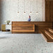 Hotel reception interior featuring Jericho Silver Terrazzo 66 × 66cm porcelain wall and floor tiles, with a soft grey base and scattered multicoloured aggregate chips, paired with warm wood panelling and minimalist lighting for a refined, contemporary setting.