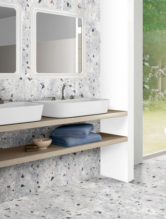 Bathroom vanity area featuring Jericho Silver Terrazzo 66 × 66cm porcelain wall and floor tiles, with a soft grey base and multicoloured aggregate chips, paired with twin basins, light wood shelving, and clean white framing for a calm, contemporary finish.