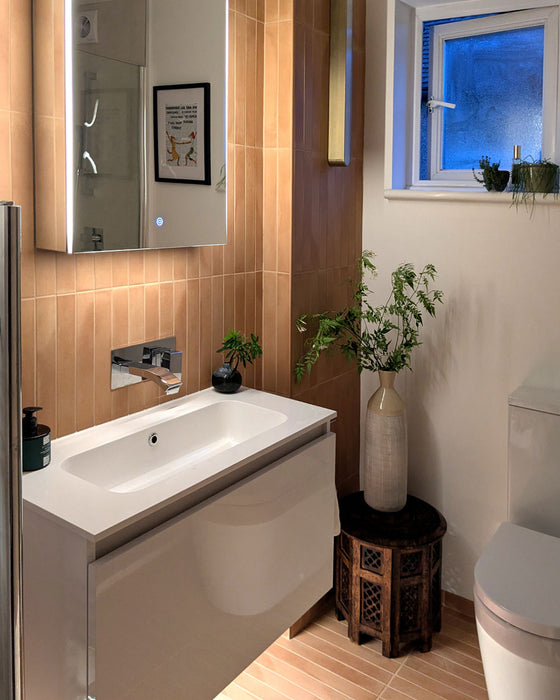 Contemporary bathroom featuring Jumairah Clay matt porcelain wall and floor tiles in a vertical stacked layout, paired with a floating white vanity, illuminated mirror cabinet, chrome brassware, soft neutral walls and natural wood accessories for a warm, minimalist interior.