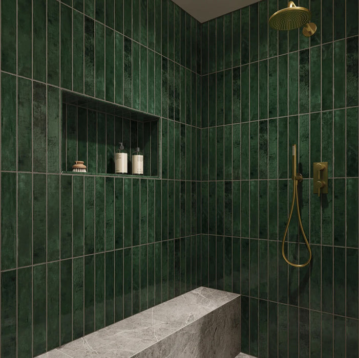 Walk-in shower featuring Jumairah Pine Forest Green 5 × 40cm gloss ceramic wall tiles, laid vertically with deep green tonal variation, paired with brass fittings, a built-in niche, and a marble-effect bench for a refined finish.