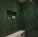Walk-in shower featuring Jumairah Pine Forest Green 5 × 40cm gloss ceramic wall tiles, laid vertically with deep green tonal variation, paired with brass fittings, a built-in niche, and a marble-effect bench for a refined finish.
