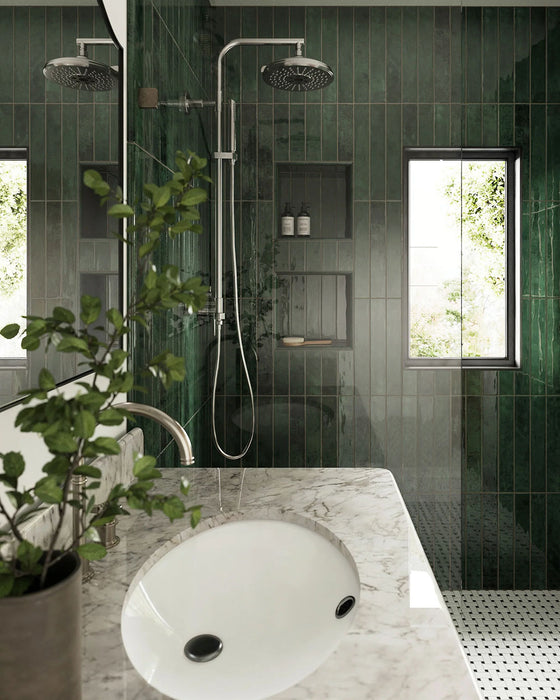 Bathroom interior featuring Jumairah Pine Forest Green 5 × 40cm gloss ceramic wall tiles, laid vertically with deep green tonal variation, paired with a marble vanity, chrome shower fittings, recessed niches, and a glass shower enclosure.