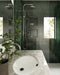 Bathroom interior featuring Jumairah Pine Forest Green 5 × 40cm gloss ceramic wall tiles, laid vertically with deep green tonal variation, paired with a marble vanity, chrome shower fittings, recessed niches, and a glass shower enclosure.