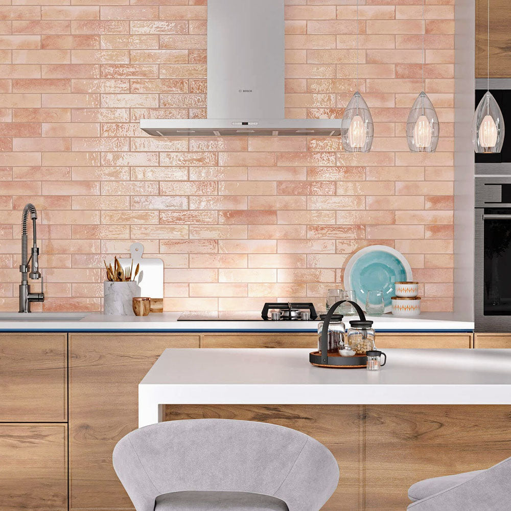 Kitchen splashback featuring Allegra Tusk Pink Gloss Brick ceramic tiles in a 6 × 25cm format, creating a warm, contemporary look with a soft pink gloss finish paired with light wood cabinetry and modern fittings.
