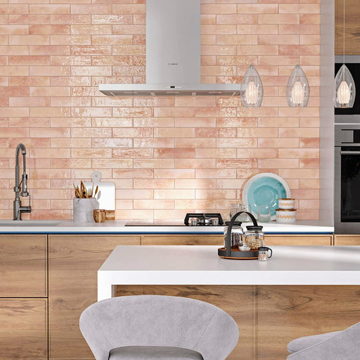 Kitchen splashback featuring Allegra Tusk Pink Gloss Brick ceramic tiles in a 6 × 25cm format, creating a warm, contemporary look with a soft pink gloss finish paired with light wood cabinetry and modern fittings.
