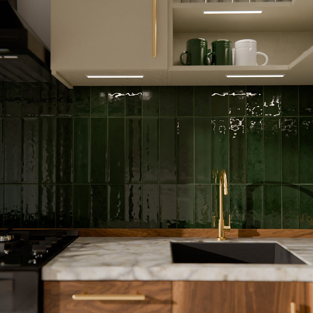 Gloss moss green Nairobi handmade-effect tiles shown in a kitchen setting, highlighting the rich colour depth and lightly textured glazed surface alongside natural wood units and brass details.