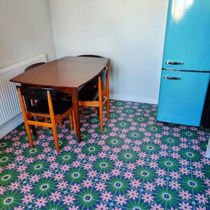 Kitchen floor featuring Fez Autumn 20x20cm Moroccan-style porcelain tiles, showcasing a vibrant geometric floral pattern in deep green, navy and blush pink tones, styled with a mid-century wooden dining table and chairs and a retro blue fridge for a bold, characterful interior.