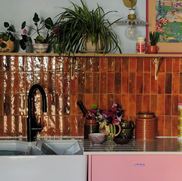 Kitchen splashback featuring Saigon Amber Brick Wall tiles in a Moroccan-inspired style, 5.1 × 16.1cm glossy ceramic tiles in warm amber tones, paired with pink cabinetry and open shelving.