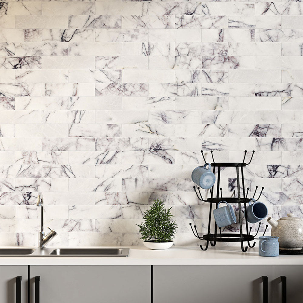 Kitchen splashback featuring Fayrouz Lilac 5x20cm natural marble tiles with a honed finish, installed in a horizontal brick layout, showcasing a soft white base with delicate lilac and grey veining, styled with neutral cabinetry, black accents, and everyday kitchen accessories for a clean, contemporary look.