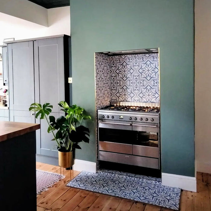 Kitchen interior featuring London Streets Thornton Place 20x20cm Victorian Moroccan style porcelain tiles used as a decorative splashback and floor detail around a range cooker, showcasing a classic blue and white patterned tile design against soft green walls and natural wood flooring.