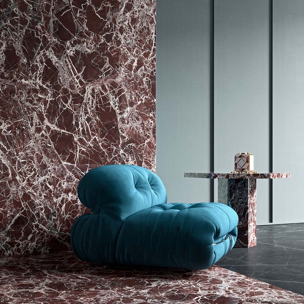 Living space featuring Levant Rouge Polished Marble effect 60 × 120cm porcelain wall and floor tiles, styled with a sculptural blue armchair, marble side table, and bold red tones with striking white veining.