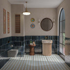 Contemporary bathroom featuring Levent Blue 6x24cm glossy brick wall tiles, with deep navy blue tones and textured glaze variation, paired with colourful Moroccan-style patterned floor tiles, a fluted cream basin, brass fittings and neutral walls.