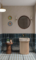 Contemporary bathroom featuring Levent Blue 6x24cm glossy brick wall tiles, with deep navy blue tones and textured glaze variation, paired with colourful Moroccan-style patterned floor tiles, a fluted cream basin, brass fittings and neutral walls.